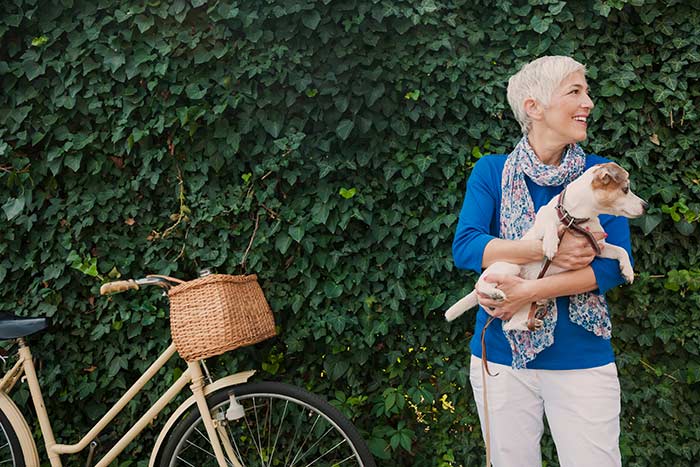 mature woman smiling in front of leafy wall while holding dog